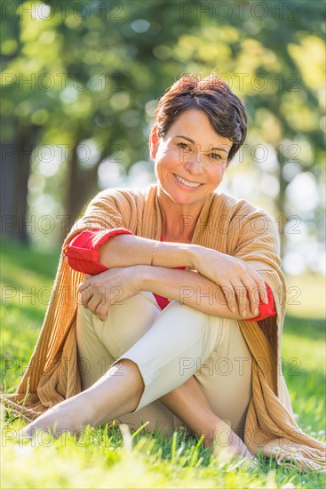 Mature woman sitting on grass in park.