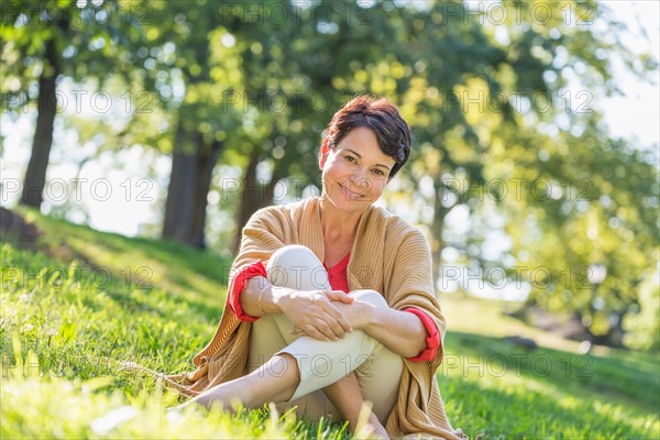 Mature woman sitting on grass in park.