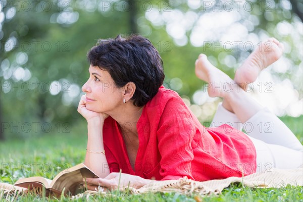 Mature woman lying on grass and reading book.