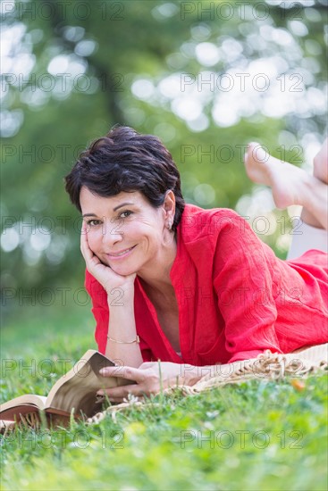 Mature woman lying on grass and reading book.