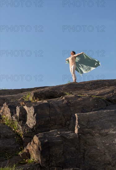 Mature woman standing on cliff with arms raised.