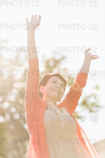 Mature woman raising hands in sunlight.