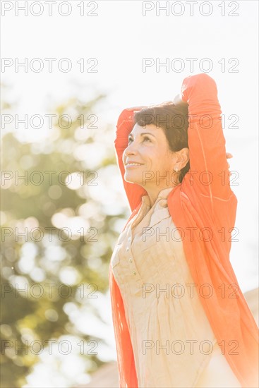 Mature woman raising hands in sunlight.