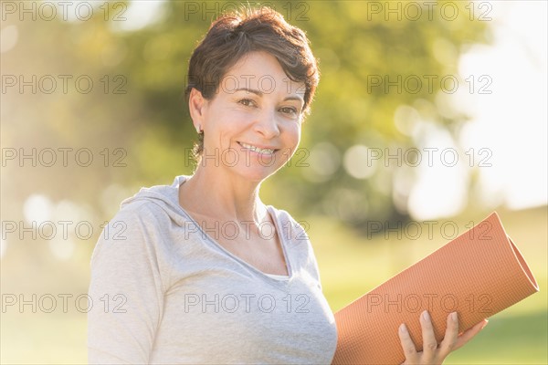 Mature woman holding yoga mat outdoors.