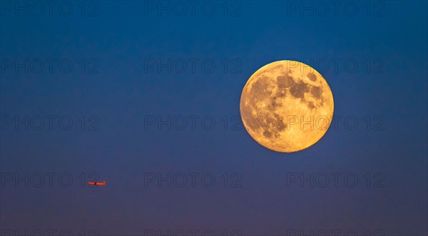 Plane flying across clear sky with full moon.