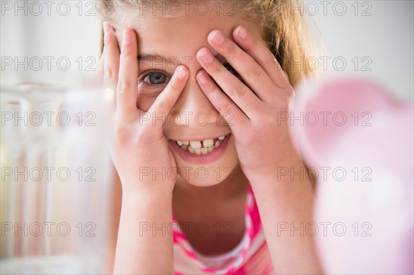 Girl (8-9) smiling and covering eyes