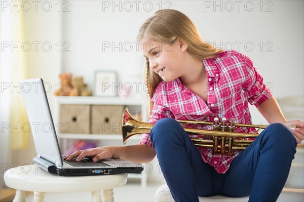 Girl (8-9) with trumpet using laptop