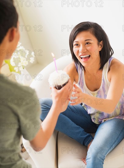Young man giving cupcake with candle to woman