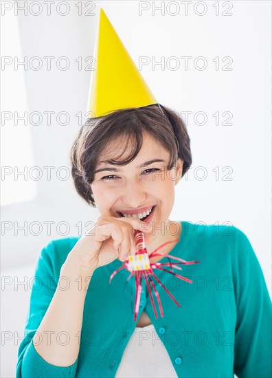 Portrait of woman wearing party hat and holding party horn blower