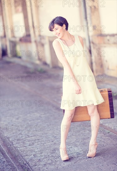 Woman in dress holding suitcase at train station