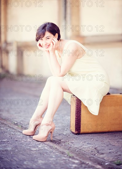Woman in dress sitting on suitcase at train station