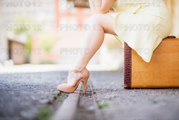 Low section of woman in dress sitting on suitcase at train station