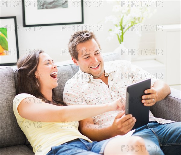 Portrait of playful couple using digital tablet on sofa