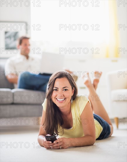 Woman lying on front and using mobile phone, man in background