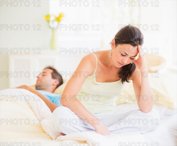 Sad woman in bedroom, man sleeping