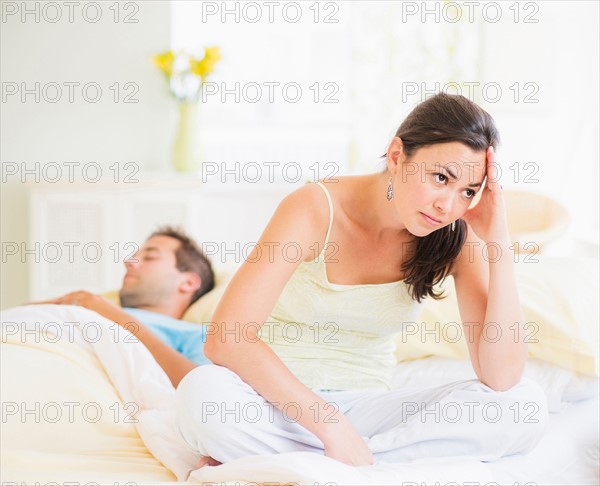 Sad woman in bedroom, man sleeping