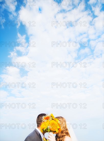 Portrait of married couple kissing behind bouquet