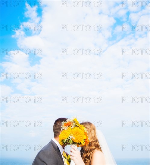 Portrait of married couple kissing behind bouquet
