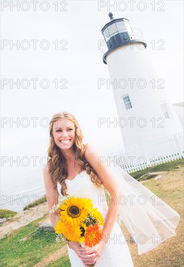 Portrait of smiling bride holding sunflower bouquet, lighthouse in background
