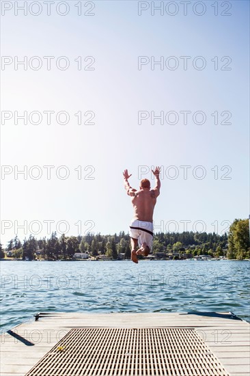 Young man jumping to lake from jetty