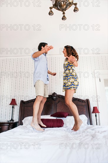 Young couple jumping on bed in hotel room