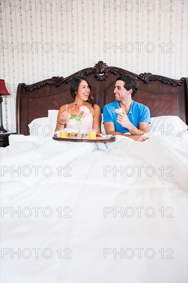 Young couple eating breakfast in bed in hotel room