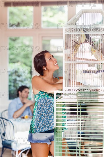 Woman standing by bird cage, man in background