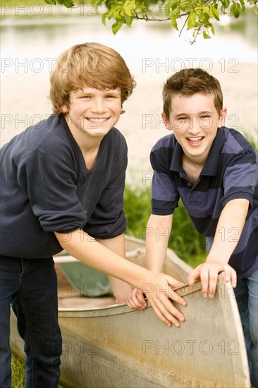 Two boys (12-13) posing with boat on grass near lake