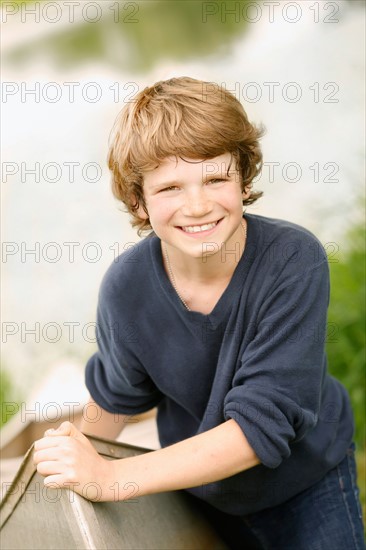 Boy (12-13) posing with boat on grass near lake