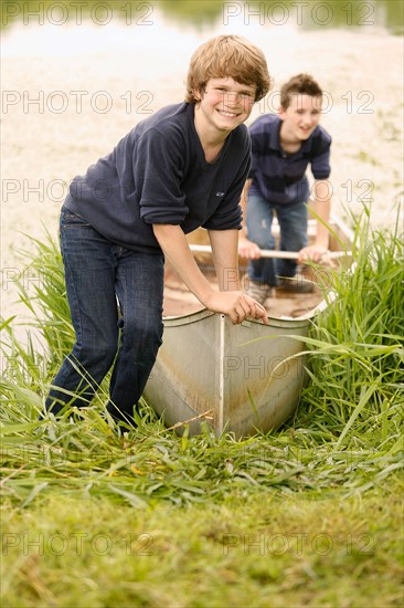 Two boys (12-13) posing with boat on grass near lake