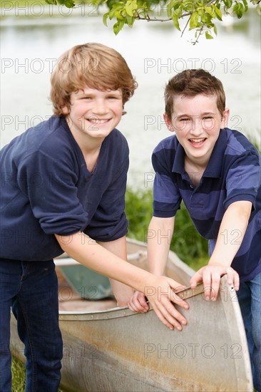 Two boys (12-13) posing with boat on grass near lake