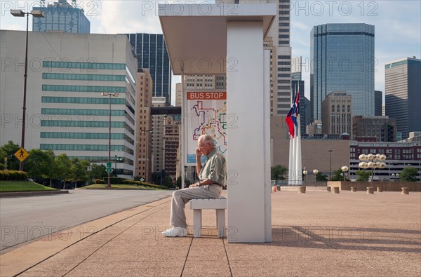 Senior man sitting at bus stop and using mobile phone