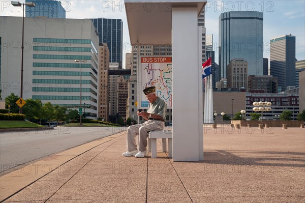 Senior man sitting at bus stop and text messaging