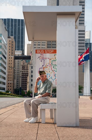 Senior man sitting at bus stop and using mobile phone