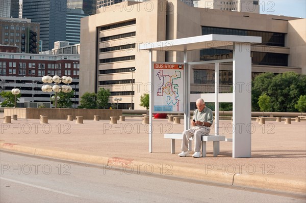 Senior man sitting at bus stop and text messaging