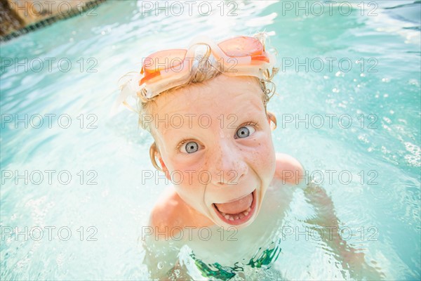 Boy (4-5) swimming in swimming pool and making funny face