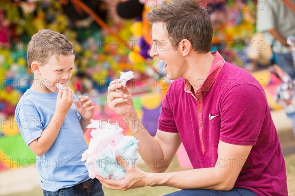 Happy father with son (4-5) in amusement park eating cotton candy