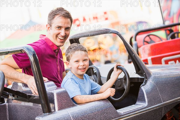 Father with son (4-5) driving toy car in amusement park