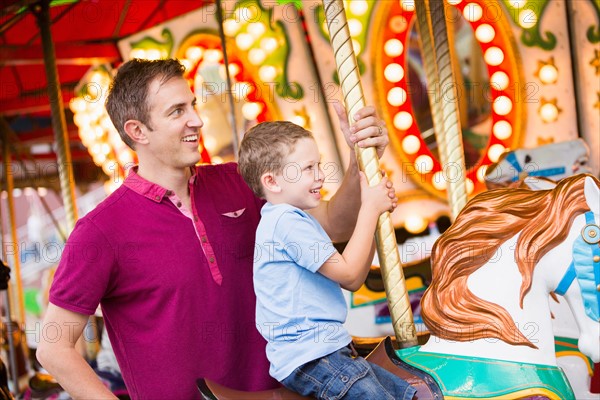Father and son (4-5) on carousel in amusement park