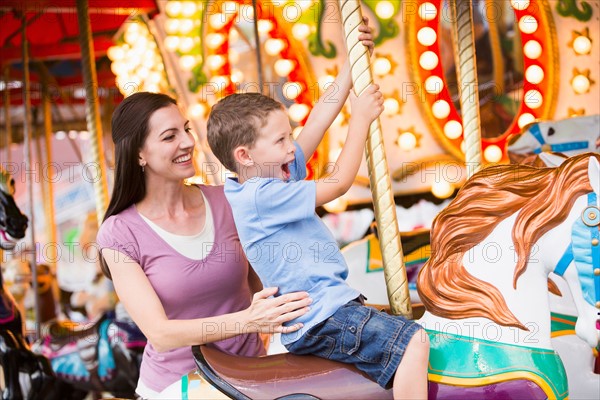 Mother and son (4-5) on carousel in amusement park