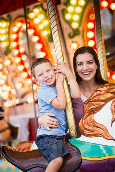 Mother and son (4-5) on carousel in amusement park