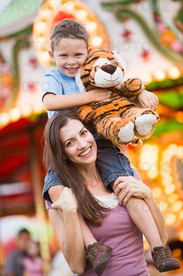 Mother giving her son (4-5) piggyback ride in amusement park