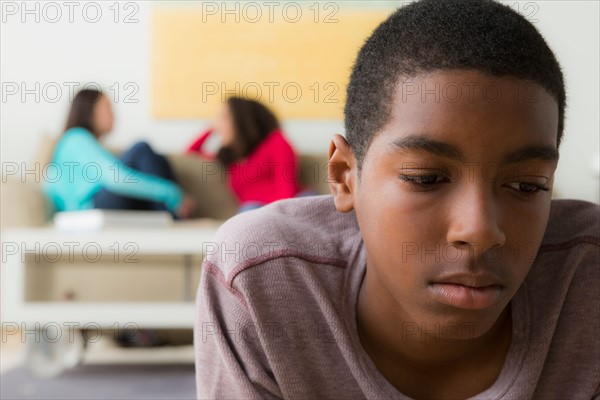 Teenage boy (14-15) crying while two friends(12-13,16-17) whispering behind her