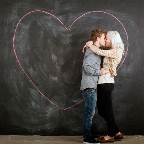 Studio portrait of young couple embracing in front of blackboard