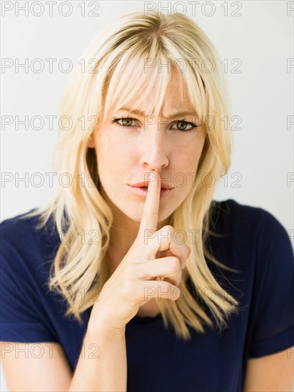 Studio portrait of blonde woman with finger on lips