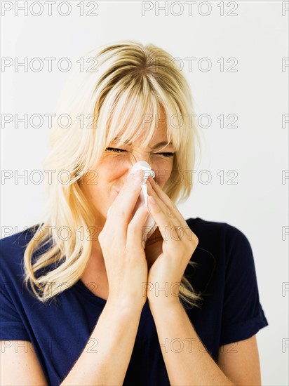 Studio portrait of blonde woman blowing nose