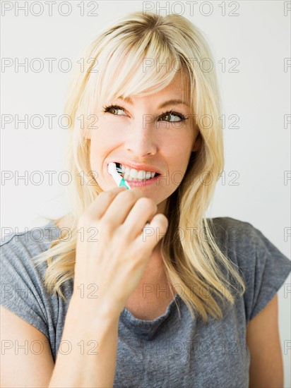 Studio portrait of blonde woman cleaning teeth
