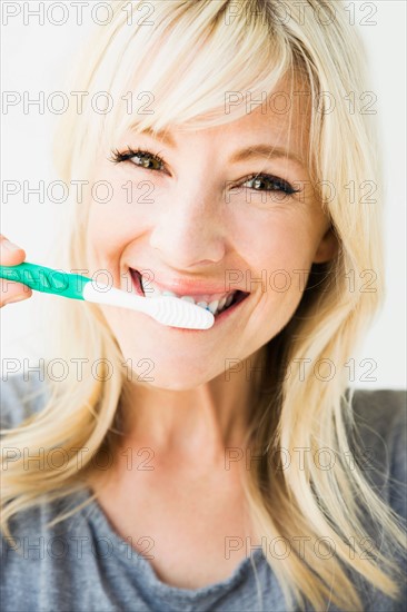 Studio portrait of blonde woman cleaning teeth