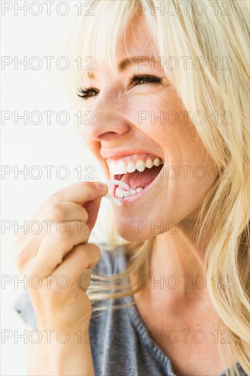 Studio portrait of blonde woman cleaning teeth with dental floss