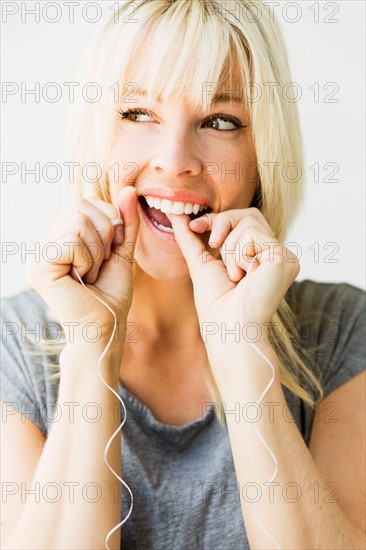 Studio portrait of blonde woman cleaning teeth with dental floss